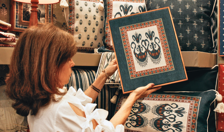 Vitrine de tecidos com almofadas estampadas e arte têxtil emoldurada em ikat nos tons verde-azulado, laranja e creme.
